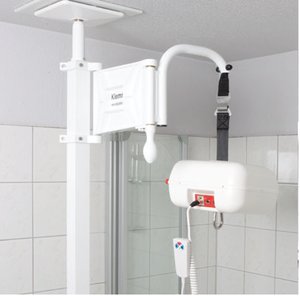Ein elektrischer Deckenlift für Patienten, bestehend aus einem an einer Teleskopstange befestigten Schwenkarm. Die Teleskopstange ist zwischen Boden und Decke verspannt, während der Schwenkarm einen motorisierten Hubmotor mit Tragband und Haken trägt. Der Lift wird über eine Handfernbedienung gesteuert und dient zum Heben und Transferieren von Personen mit eingeschränkter Mobilität.