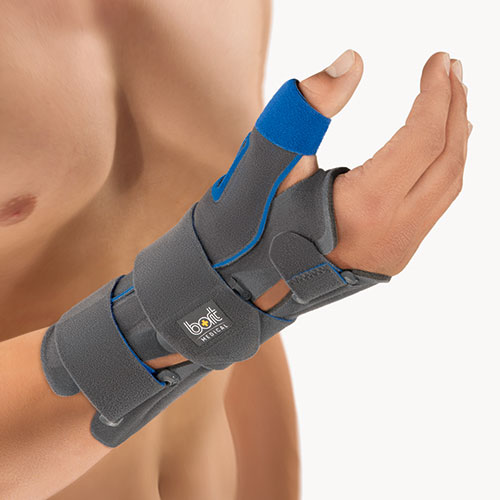 Diese Nahaufnahme zeigt eine graue Handgelenk-Daumen-Orthese, die an der rechten Hand eines Mannes mit nacktem Oberkörper getragen wird. Die Schiene ist aus einem festen, grauen Material gefertigt und verfügt über blaue Klettverschlüsse und Zierelemente, die für einen sicheren Halt sorgen. Sie bedeckt einen großen Teil des Unterarms, das Handgelenk und umschließt den Daumen, um diesen zu stabilisieren, während die restlichen Finger frei beweglich bleiben. Die Hand ist leicht angewinkelt und entspannt, um die Funktionalität und den Tragekomfort der Orthese zu demonstrieren.