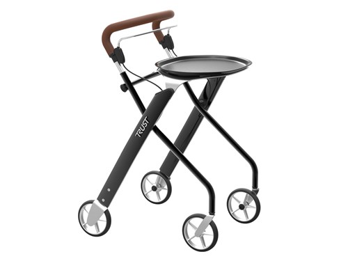 Ein eleganter Indoor-Rollator der Marke Trust mit einem schmalen, schwarz-silbernen Gestell und vier kleinen Rädern vor weißem Hintergrund. Das Design zeichnet sich durch einen durchgehenden, braunen Schiebebügel in Lederoptik und einen darunter liegenden Bremsbügel aus. Auf der Oberseite des Gestells ist ein praktisches, rundes Tablett in Schwarz zum Transport von Gegenständen montiert. Die X-förmige Rahmenkonstruktion wirkt besonders modern und ist speziell für die Nutzung in Innenräumen konzipiert.