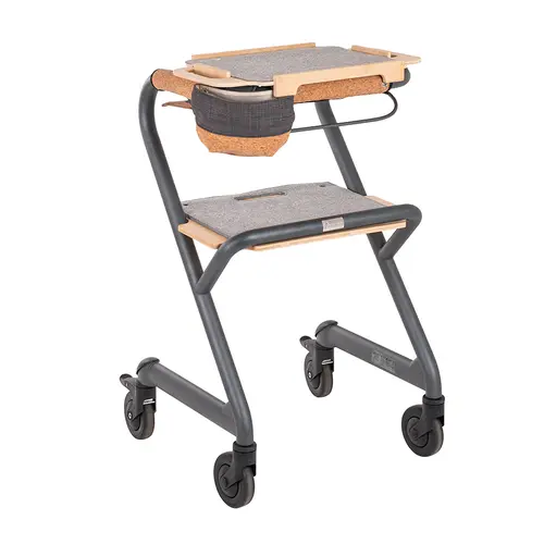 Ein moderner, grauer Indoor-Rollator mit Holz- und Korkakzenten, einem Tablett oben, einem Sitz in der Mitte und einer angehängten Stofftasche auf weißem Hintergrund.